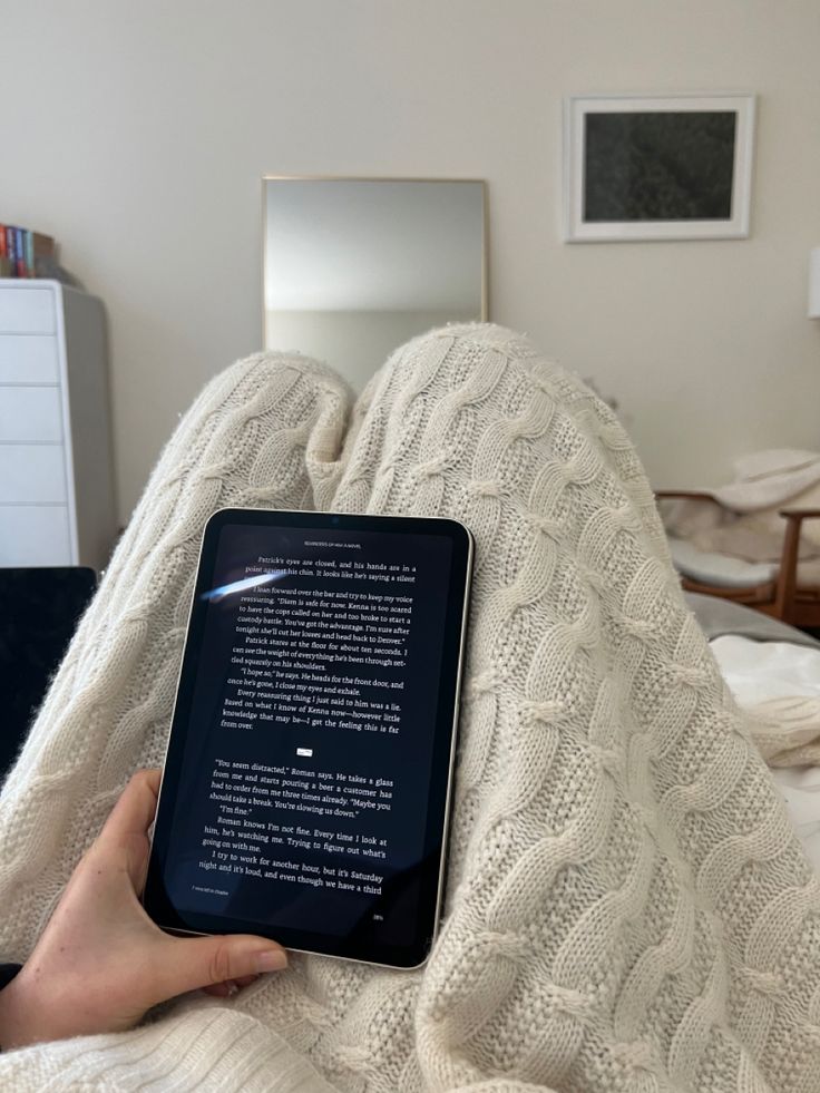 a person is laying in bed with a book on their lap and holding it up to the camera