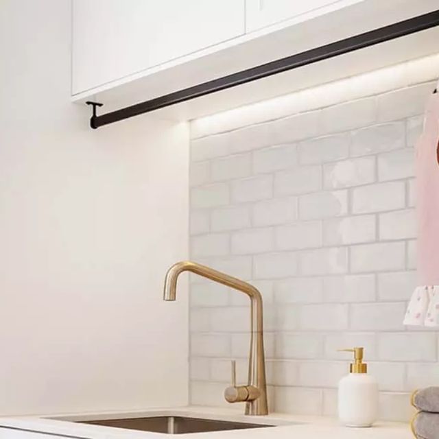 a kitchen with white counter tops and gold faucet, pink towel hanging on the wall