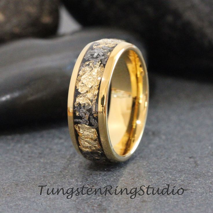 a wedding ring with gold and black wood inlays on it, sitting next to some rocks