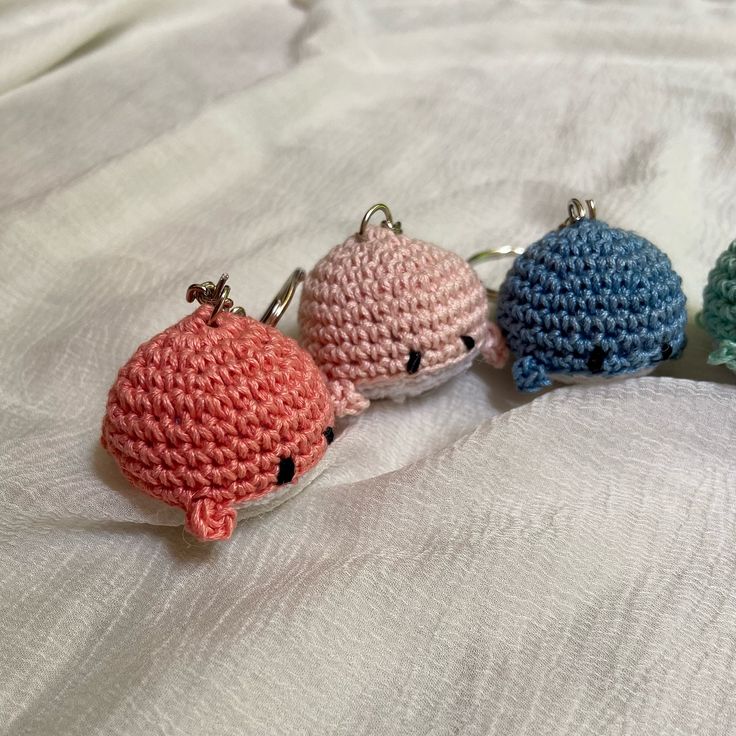 three crocheted keychains sitting on top of a white bed covered in sheets