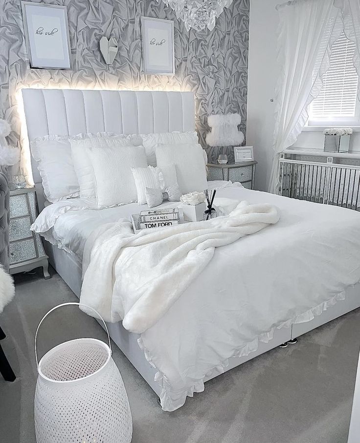 a white bed in a bedroom next to a wall with pictures on it and a chandelier