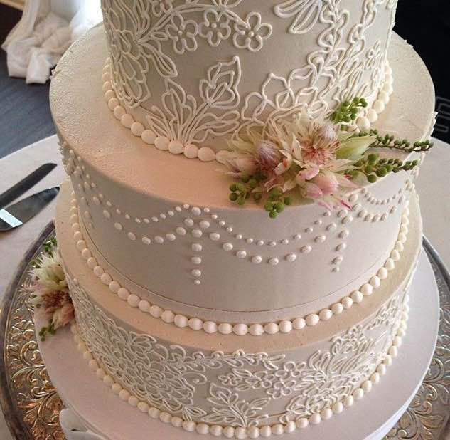 a three tiered wedding cake with flowers and pearls on the bottom, sitting on a silver platter