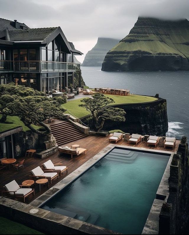 an outdoor swimming pool with chaise lounges next to it and the ocean in the background