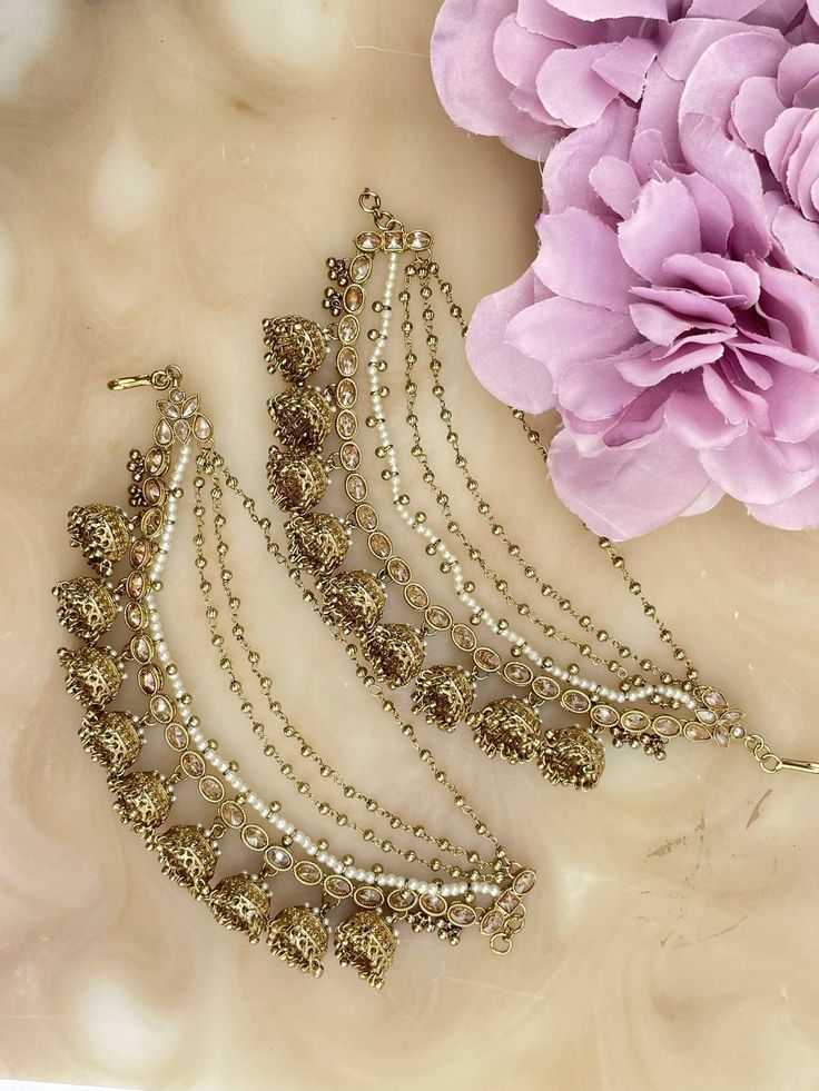 These 5 tiered beautiful jhumki sahara are the perfect accessory to finish off any party look. The sahara come in a pair and are universal and reusable, they can be easily attached to the back of any earring, making them a versatile accessory that you can use with any earring. The sahara feature a beautiful large jhumki design on the bottom tier, which adds a touch of elegance and sophistication to the accessory. The four tiers of the sahara drape perfectly and are adorned with small white pearls and antique gold beads that create a delicate look. The jhumkis are also finished off with pearl work that adds a touch of elegance and shimmer to the accessory. These sahara are perfect for any special occasion, including weddings, receptions, and parties. They are designed to add a touch of glam Traditional Tikka With Latkans For Party, Navratri Party Tikka With Latkans, Party Tikka With Latkans For Navratri, Adjustable Tikka For Diwali Party, Eid Party Tikka With Latkans, Adjustable Tikka For Festivals, Adjustable Bollywood Style Tikka For Parties, Bohemian Tilla Tikka For Diwali, Festive Celebration Tikka With Latkans