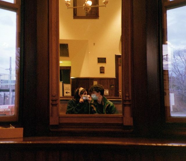 two people are taking pictures in the mirror with their cell phones while sitting at a table