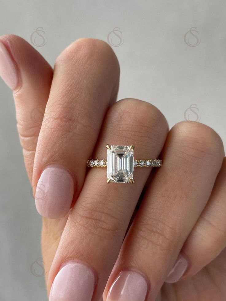 a woman's hand holding an emerald and diamond ring