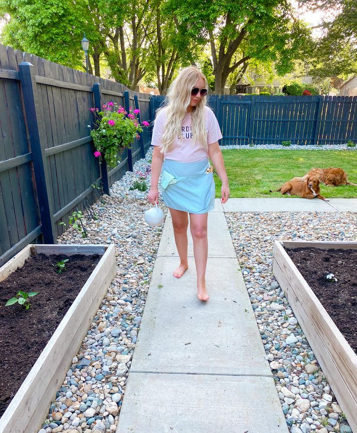 a woman walking down a sidewalk next to a garden