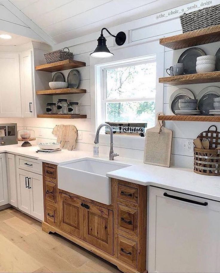 a white kitchen with wooden cabinets and open shelvings on the wall above the sink