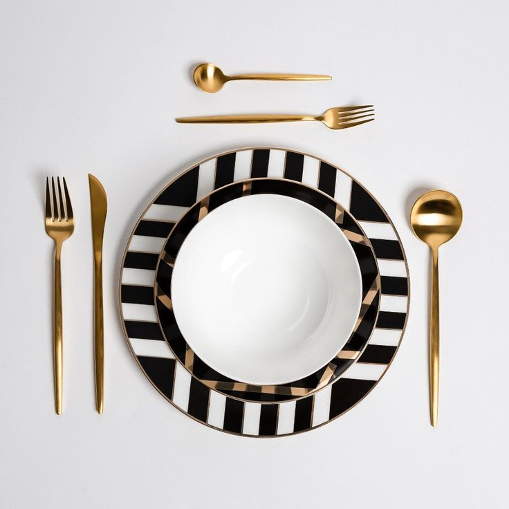 a black and white plate with gold forks, spoons and knives on it next to a bowl