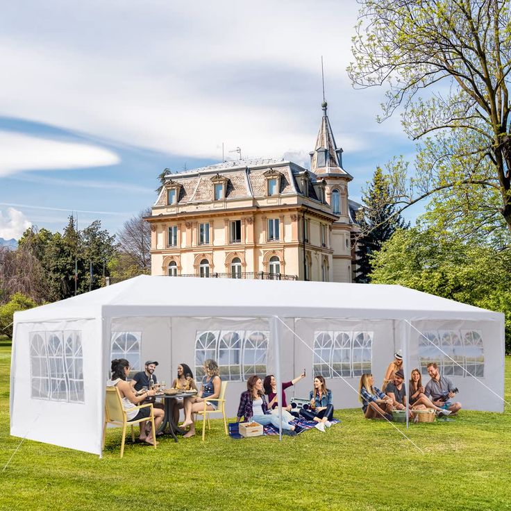 a group of people sitting in chairs under a tent on the grass near a building