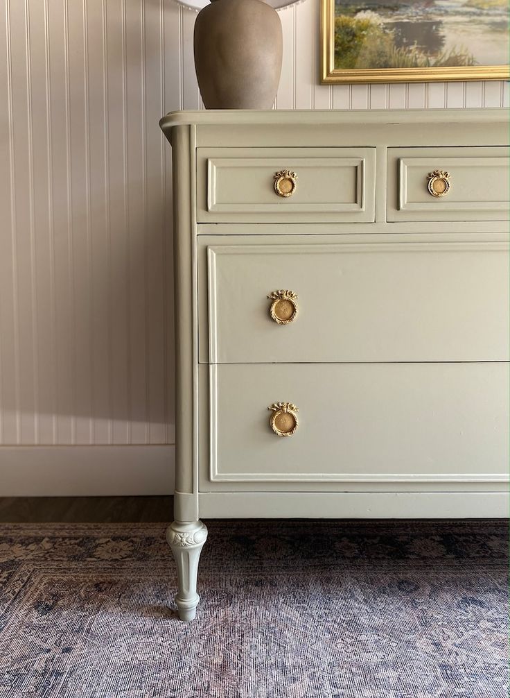 a white dresser with gold handles and knobs in a room next to a painting on the wall