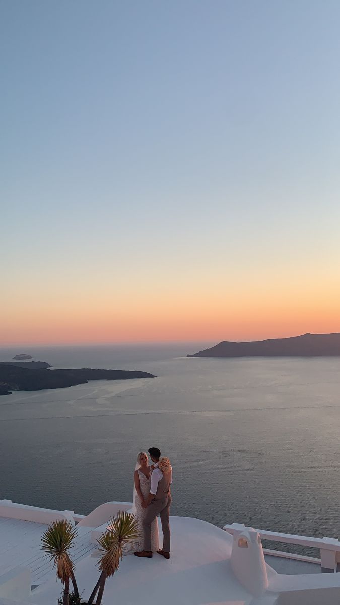 two people standing on top of a snow covered roof next to the ocean at sunset