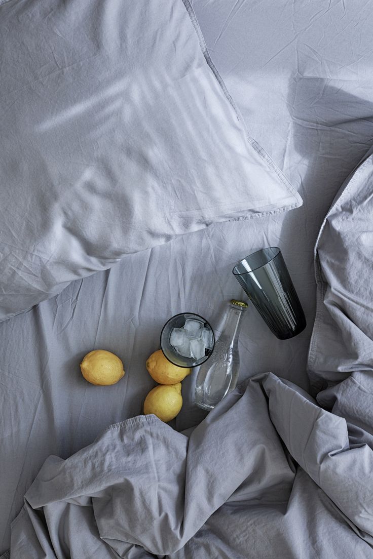 an unmade bed with white sheets and gray linens has lemons on it