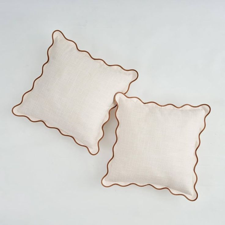 two pillows with scalloped edges on a white surface, one is beige and the other is brown