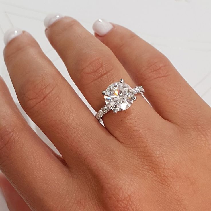 a woman's hand with a diamond ring on top of her finger and white nails