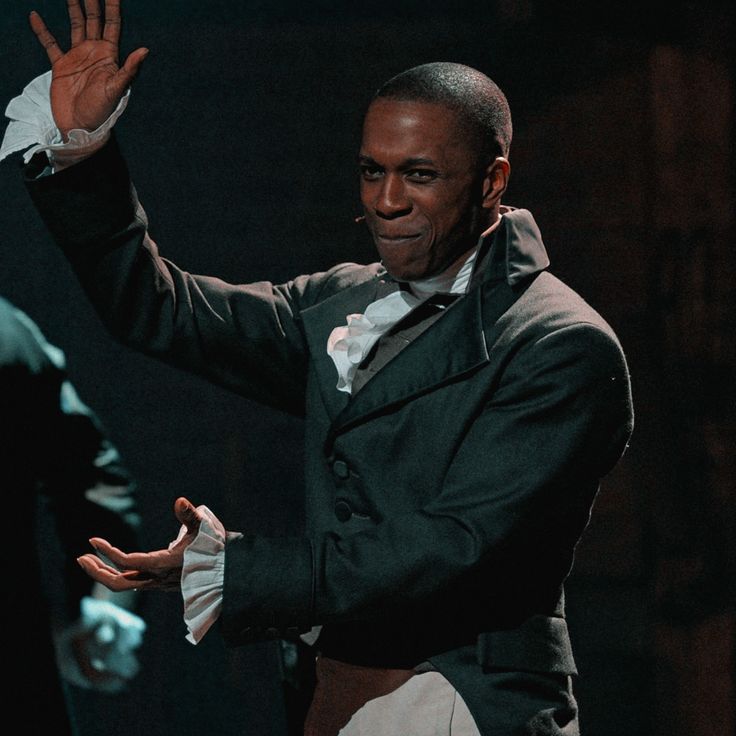 a man in a tuxedo waves to the crowd as he stands on stage