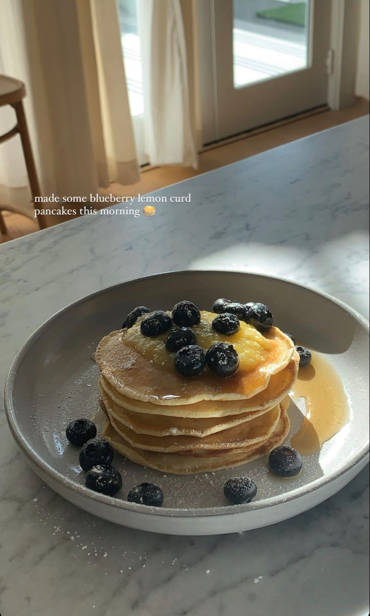 stack of pancakes with blueberries and syrup on a marble countertop in front of a window