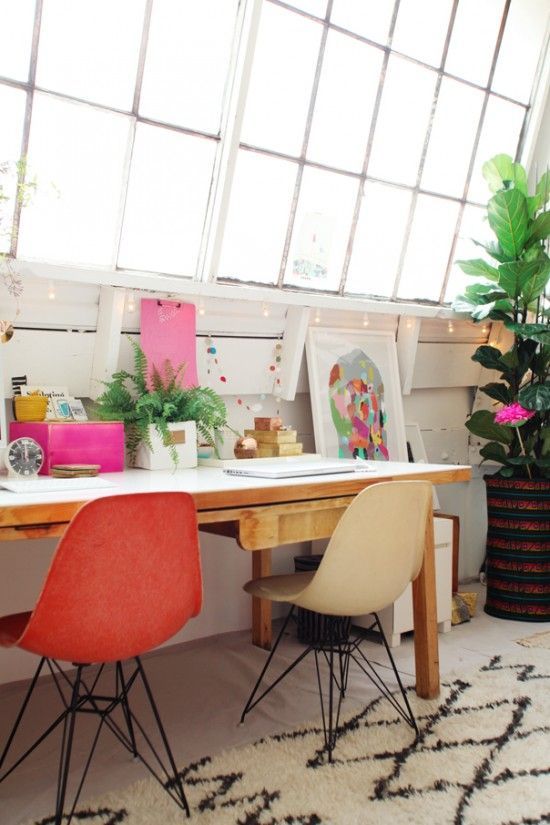 two chairs are sitting at a table with pictures on the wall and plants in pots