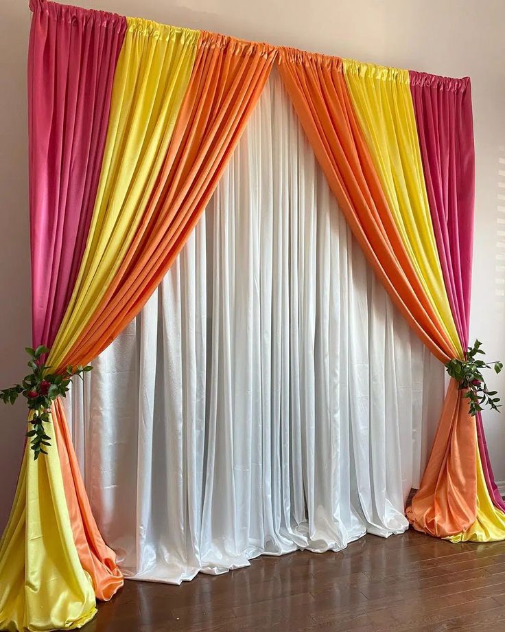 an orange, yellow and pink drapes are hanging on the wall next to a wooden floor