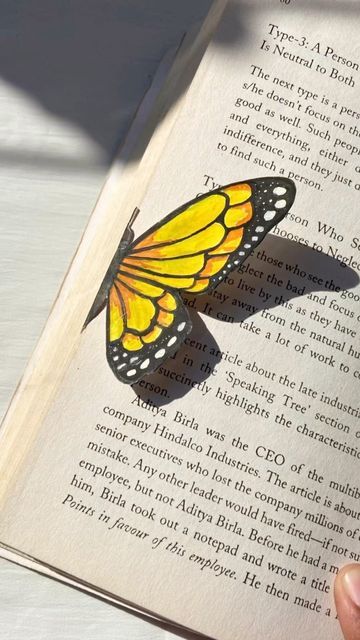 a person holding an open book with a butterfly on it's cover and the pages are yellow