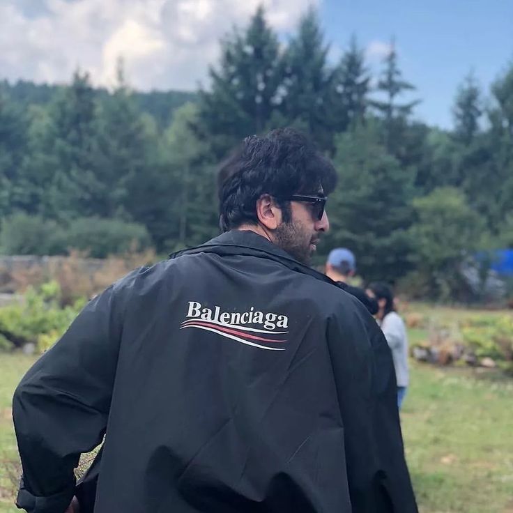 a man wearing a black jacket with the word balenodiaa on it is standing in a field