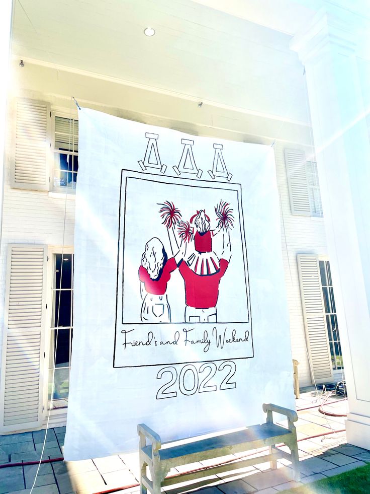 a white banner hanging from the side of a building next to a wooden bench and windows