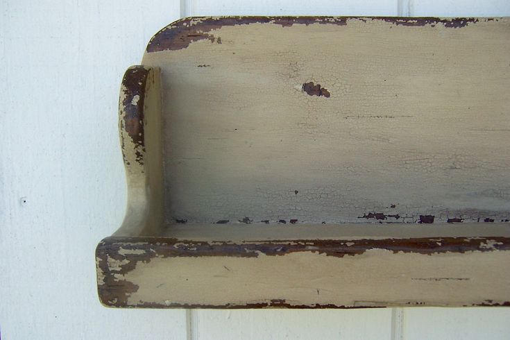 an old wooden shelf hanging on the side of a white building with peeling paint and chipped paint