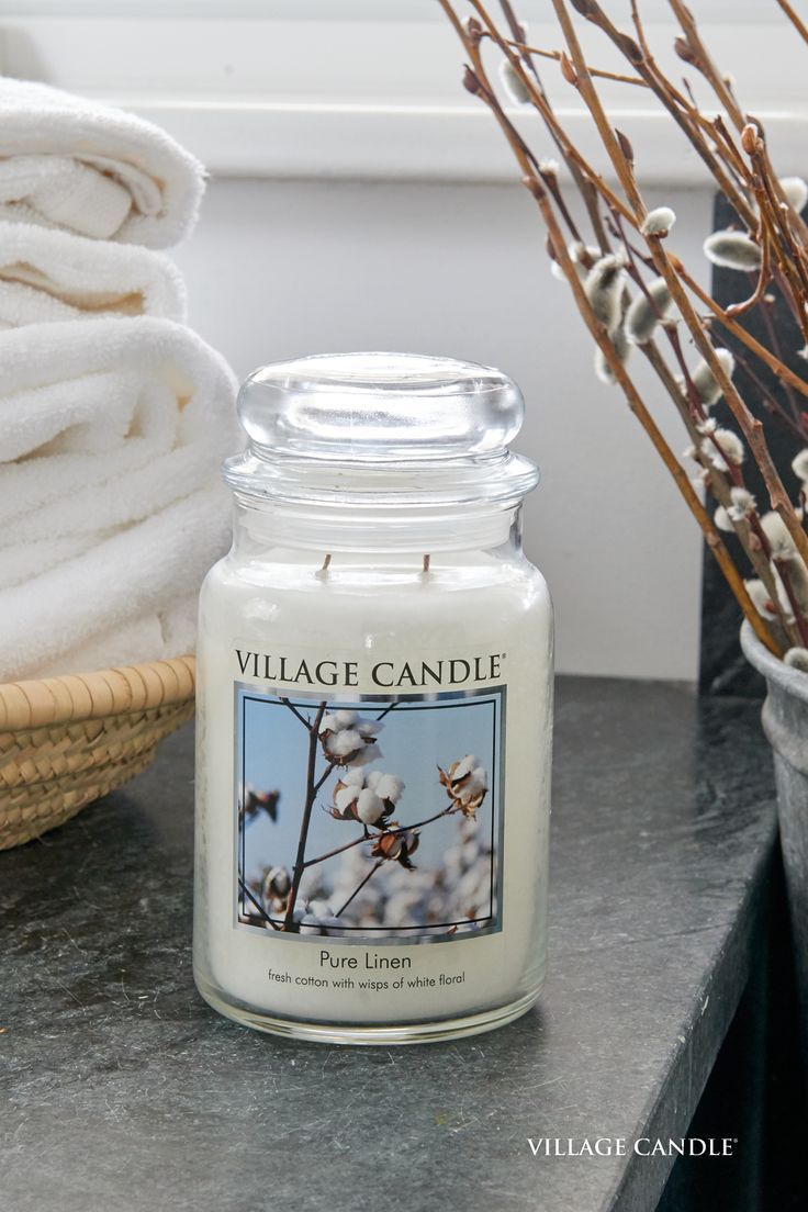 a white candle sitting on top of a counter next to a basket filled with towels