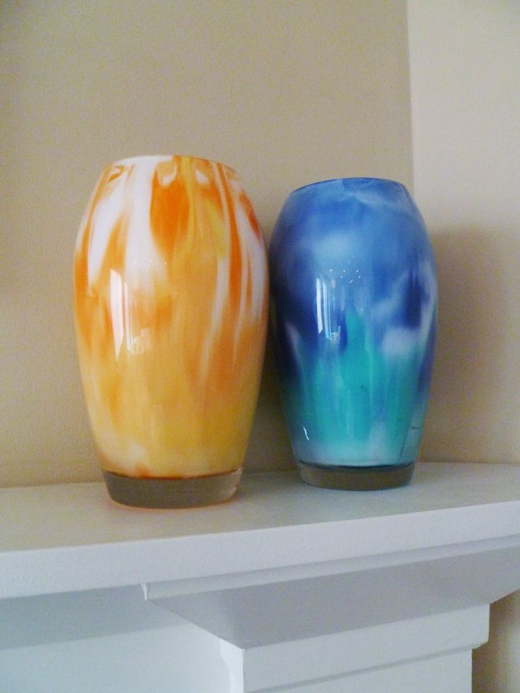 two colorful vases sitting on top of a white shelf next to eachother