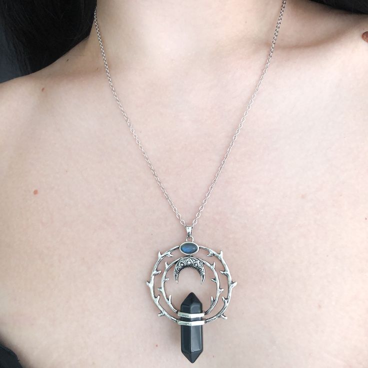 Thorns tell the beholder to love a beauty but from a safe distance. For if they come to pluck her beauty she will scratch back. Our magical circle of thorns hold a protective obsidian stone with a floating crescent moon above it under a labradorite stone. Labradorites enhance intuition. Our chain is 18" long with a 3" extension for additional length. Recycled brass base with a darker silver finish. Stones are genuine gemstone. All orders over $50 ship for free within the USA. All orders usually Black Labradorite Spiritual Necklaces, Mystical Round Pendant Metal Jewelry, Black Moon Charm Jewelry For Festivals, Black Moon Phase Necklaces For Festival, Mystical Metal Round Pendant Jewelry, Black Moon Phase Necklace For Festival, Black Jewelry With Moon Charm For Festivals, Black Crescent Jewelry For Festival, Black Labradorite Jewelry For Gift