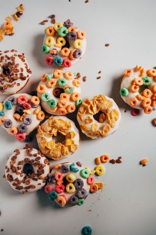 several donuts with cereal and cereal toppings scattered around them on a white surface