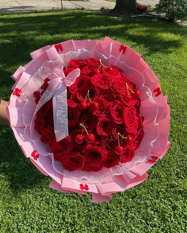 a person holding a large bouquet of red roses in the grass with a ribbon tied around it