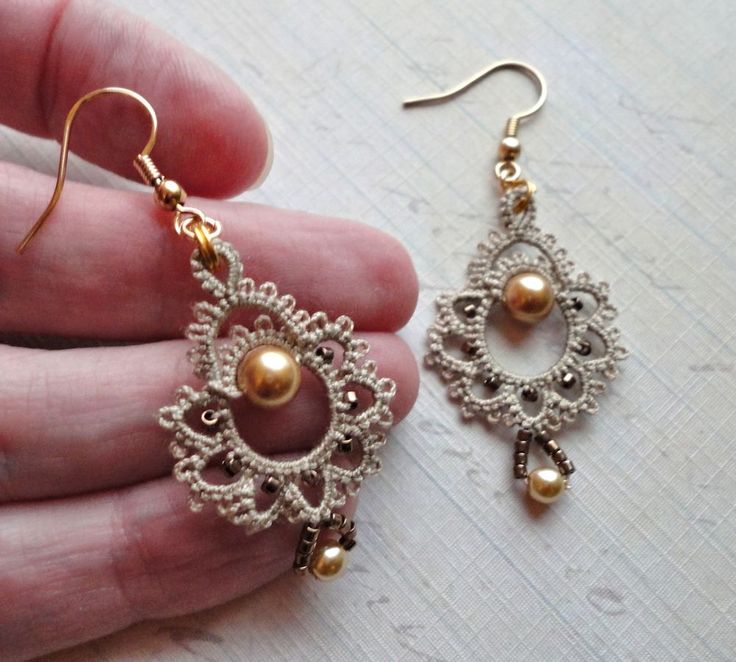 a pair of gold and white earrings in someone's hand, with pearls hanging from them