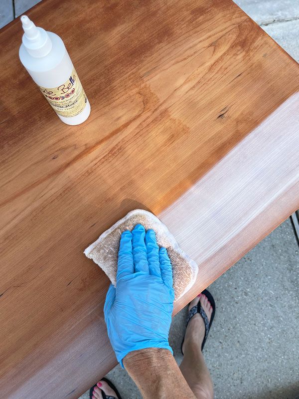 a person in blue gloves wiping up a wooden table