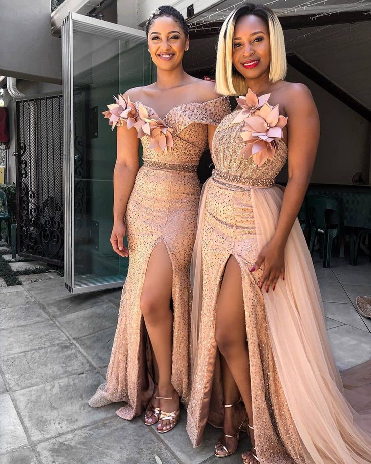 two women standing next to each other wearing dresses with high slits and flowers on them