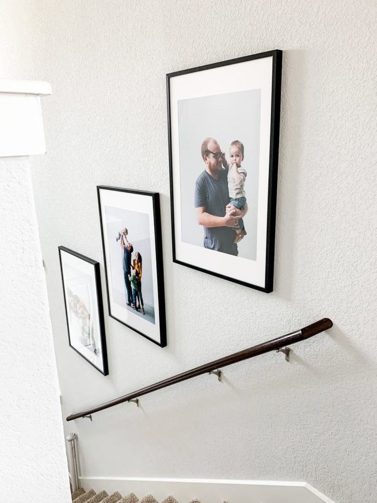 three framed photos hang on the wall above a stair case with two people holding a baby