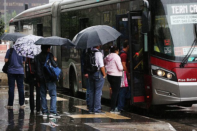 people standing on the sidewalk with umbrellas waiting to board a bus in the rain