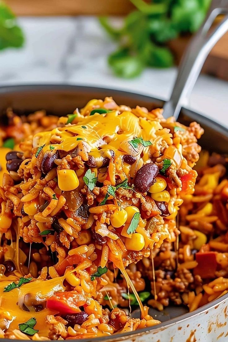 a spoon full of mexican rice with beans and cheese on top, in a skillet