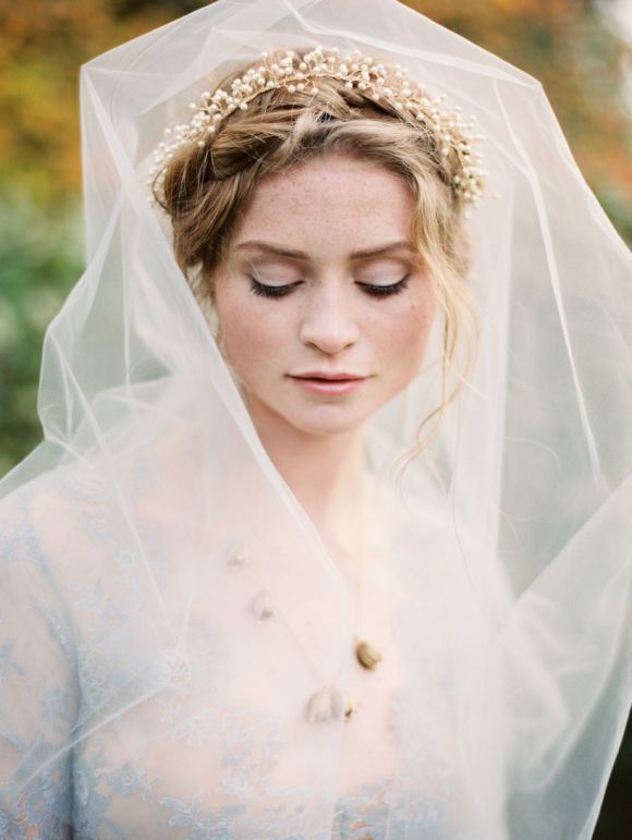 a woman wearing a veil and headpiece with flowers in her hair is looking down