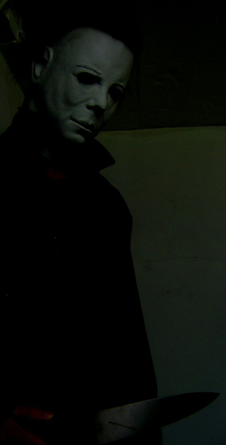 a man with a knife in his hand and a creepy mask over his face, standing next to a wall