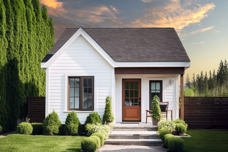 a small white house surrounded by trees and grass with a wooden door on the front