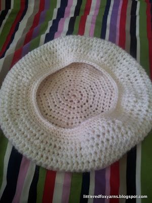 a white crocheted hat sitting on top of a striped bed sheet with stripes