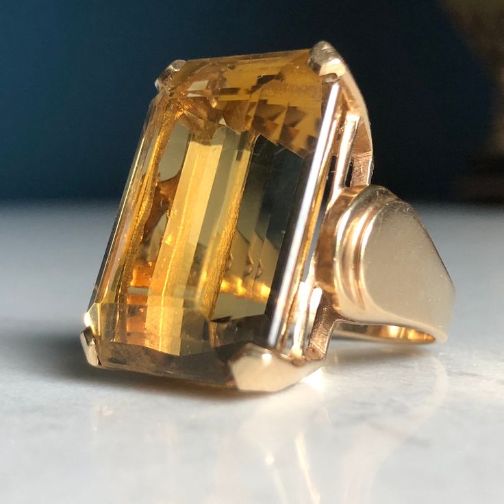 14k Stamped & tested yellow gold cast Citrine Quartz statement ring with a bright polish finish. This contemporary art-deco style fashion ring features a top center four- prong basket head-set emerald-shape step-cut citrine quartz with layered rolling cathedral shoulders. Ring measures approximately 20.00mm at the base of the top and approximately 9.50 wide at the wildest point of each shoulder tapering to approximately 2.78mm wide at the bottom of the shank. Ring size is: 5 3/4 Containing: One prong set emerald step cut natural citrine quartz. Measuring 24.00 x 17.50 x 11.66mm, (depth set). Approximate weight of 35.17ct, Clarity is eye clean, medium light, moderately strong, organgy yellow color, very good cut. Total Weight of Colored Stones:  36.17ct Total Weight of Ring:  16.28grams *20 Luxury Gold Faceted Rings, Luxury Yellow Gold Timeless Crystal Ring, Luxury Timeless Yellow Gold Crystal Ring, Luxury Yellow Gold Crystal Ring With Center Stone, Luxury Gold-tone Metal Ring, Luxury Faceted Yellow Gold Rings, Luxury Yellow Gold Emerald-cut Crystal Ring, Citrine Ring Engagement, Dream Rings