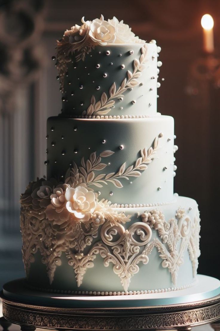 a three tiered blue wedding cake with white flowers and pearls on the top layer