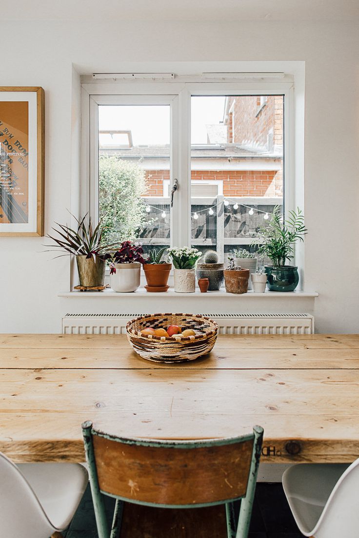 a wooden table sitting under a window next to two white chairs and a potted plant