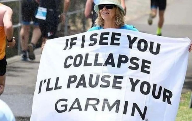 a woman holding a sign that says if i see you collapse i'll pause your garmin