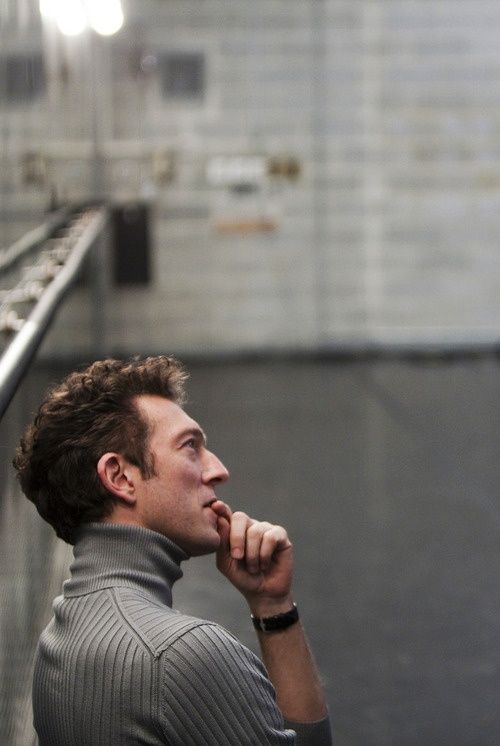 a man standing in front of a metal railing with his hand on his chin and looking off into the distance