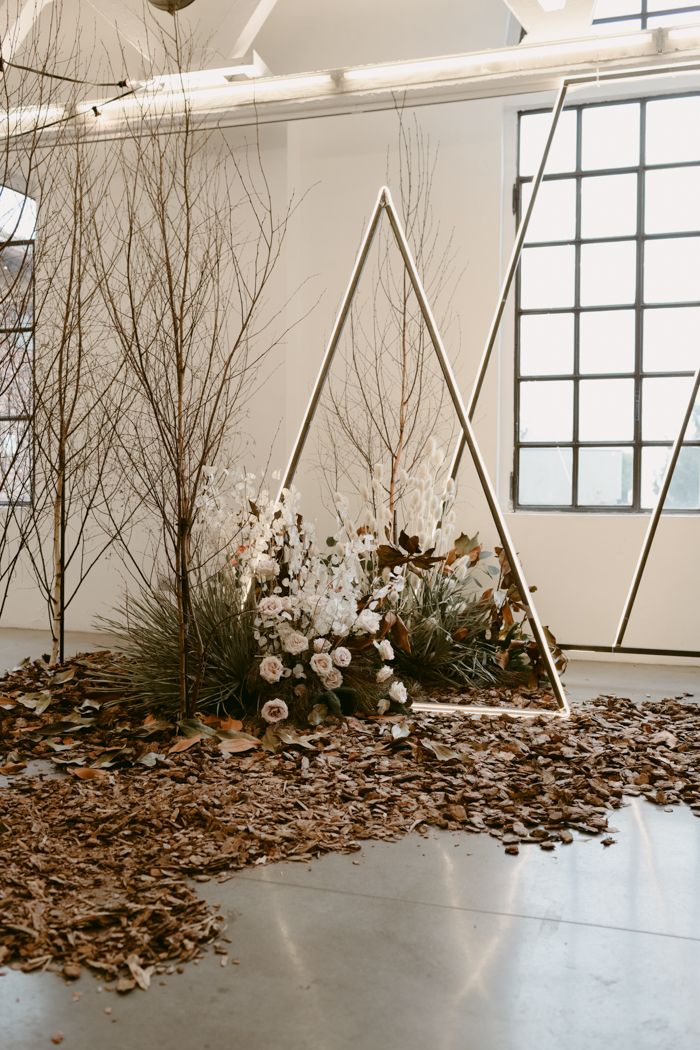 an arrangement of branches and flowers on the floor in front of a wall with geometric shapes