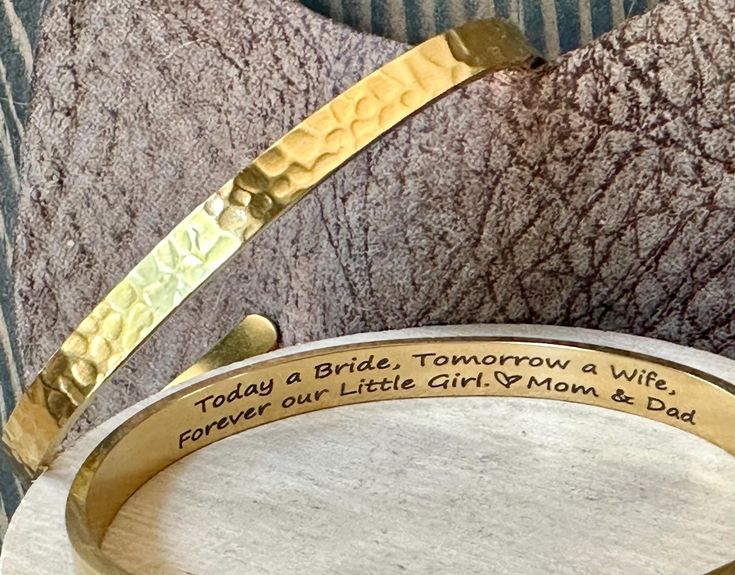 a close up of a bracelet with writing on the side and two pieces of gold colored metal