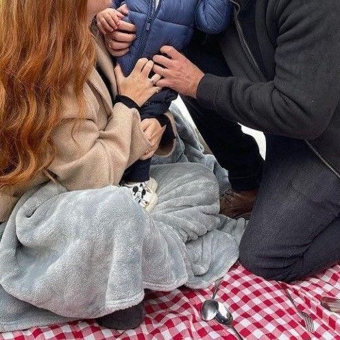 a man and woman holding a baby on top of a picnic table next to each other